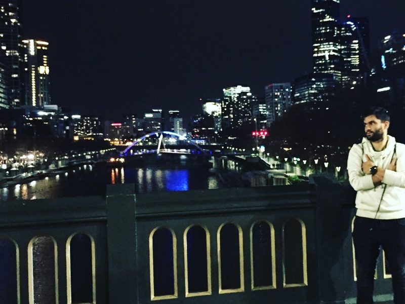 chico joven en un puente y mirando la ciudad de Melbourne de noche iluminada